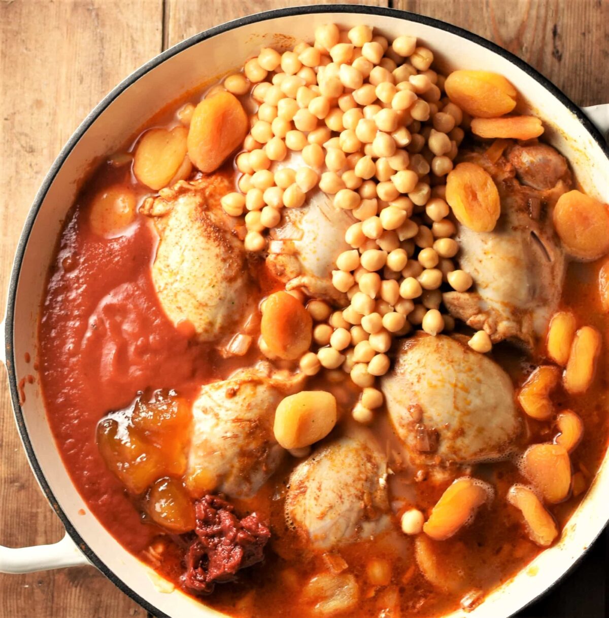 Top down view of chicken, chickpeas, dried apricots in tomato sauce in large shallow dish.