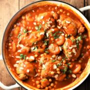 Chicken with chickpeas in tomato sauce with almond flakes in shallow white dish.