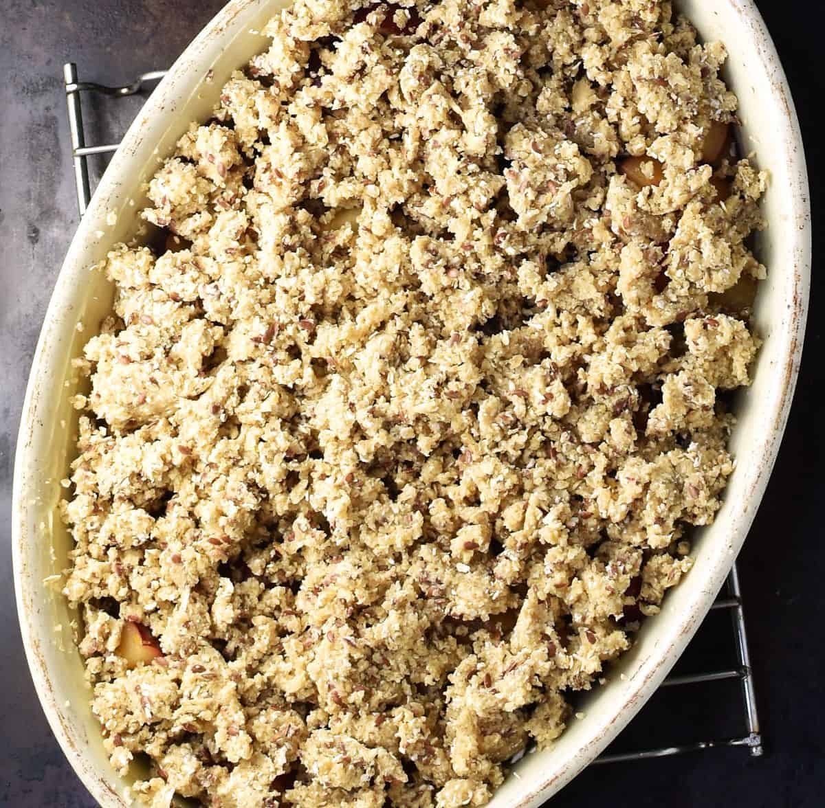 Top down view of assembled plum crumble in white oval dish.