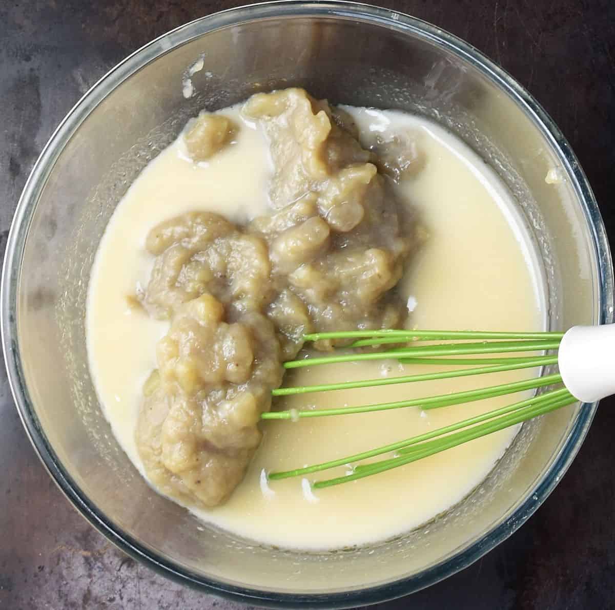 Egg mixture with cooked fruit in glass bowl with whisk.