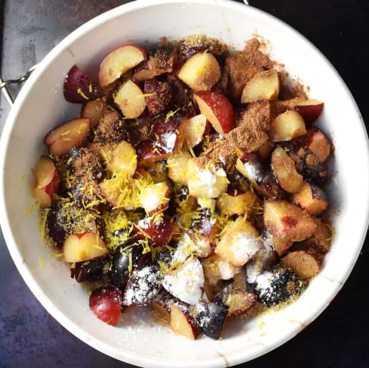 Pieces of plums with flour and spice in white bowl.