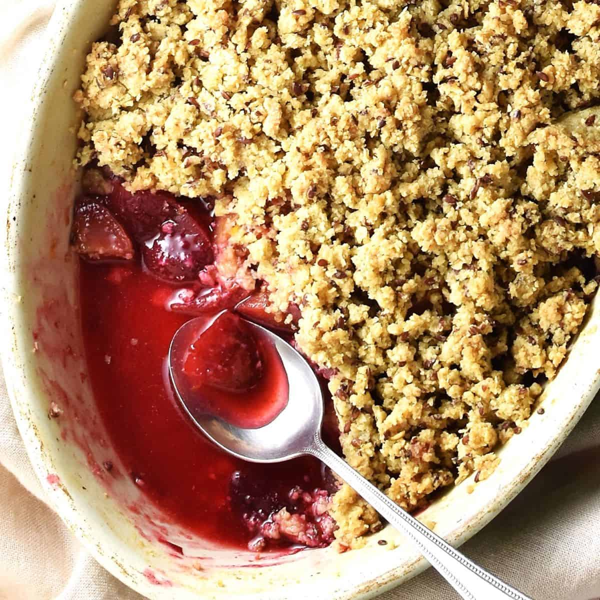 Partial top down view of vegan plum crumble with spoon in oval dish.