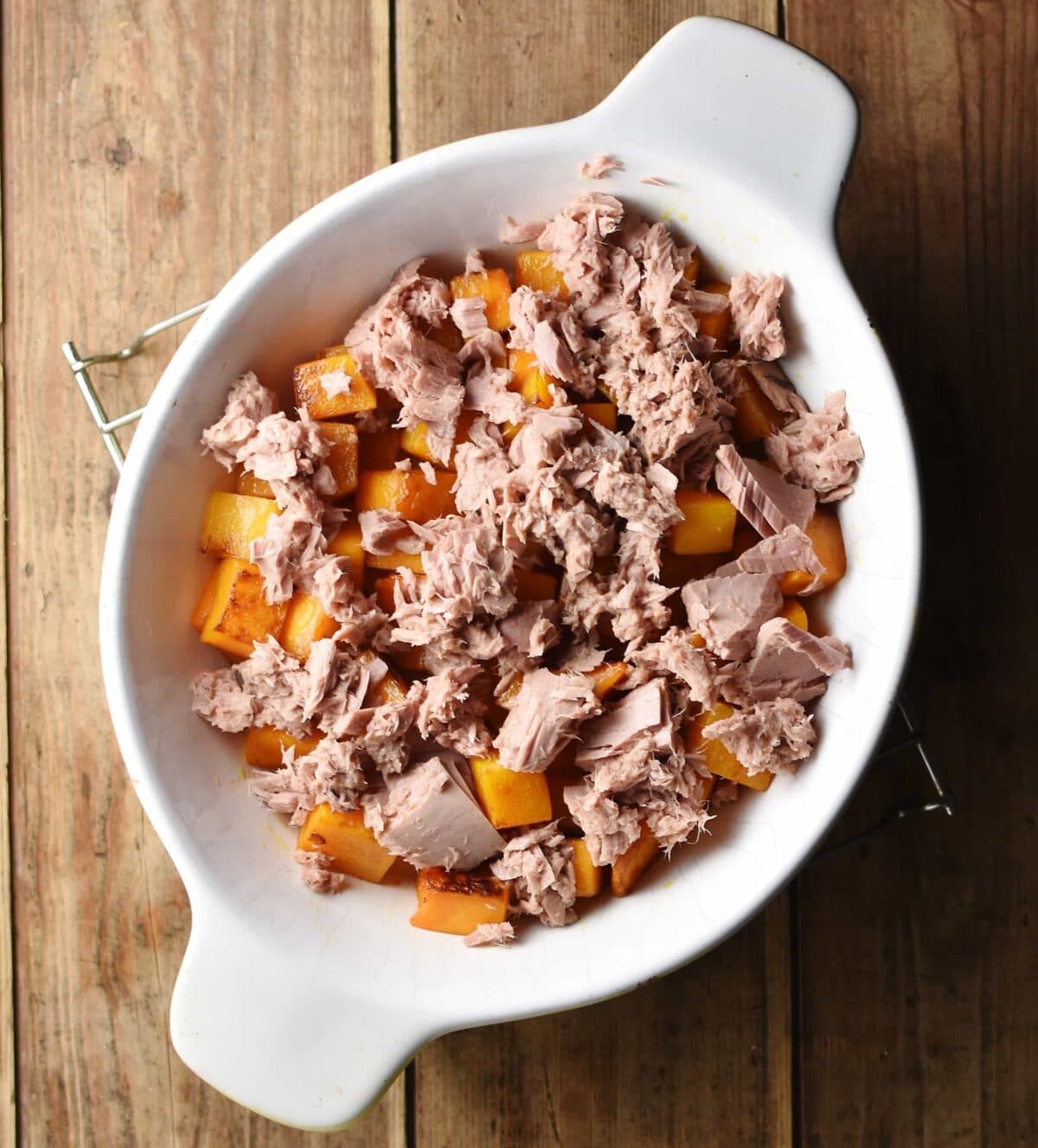 Tuna chunks scattered over squash cubes inside white oval casserole dish.