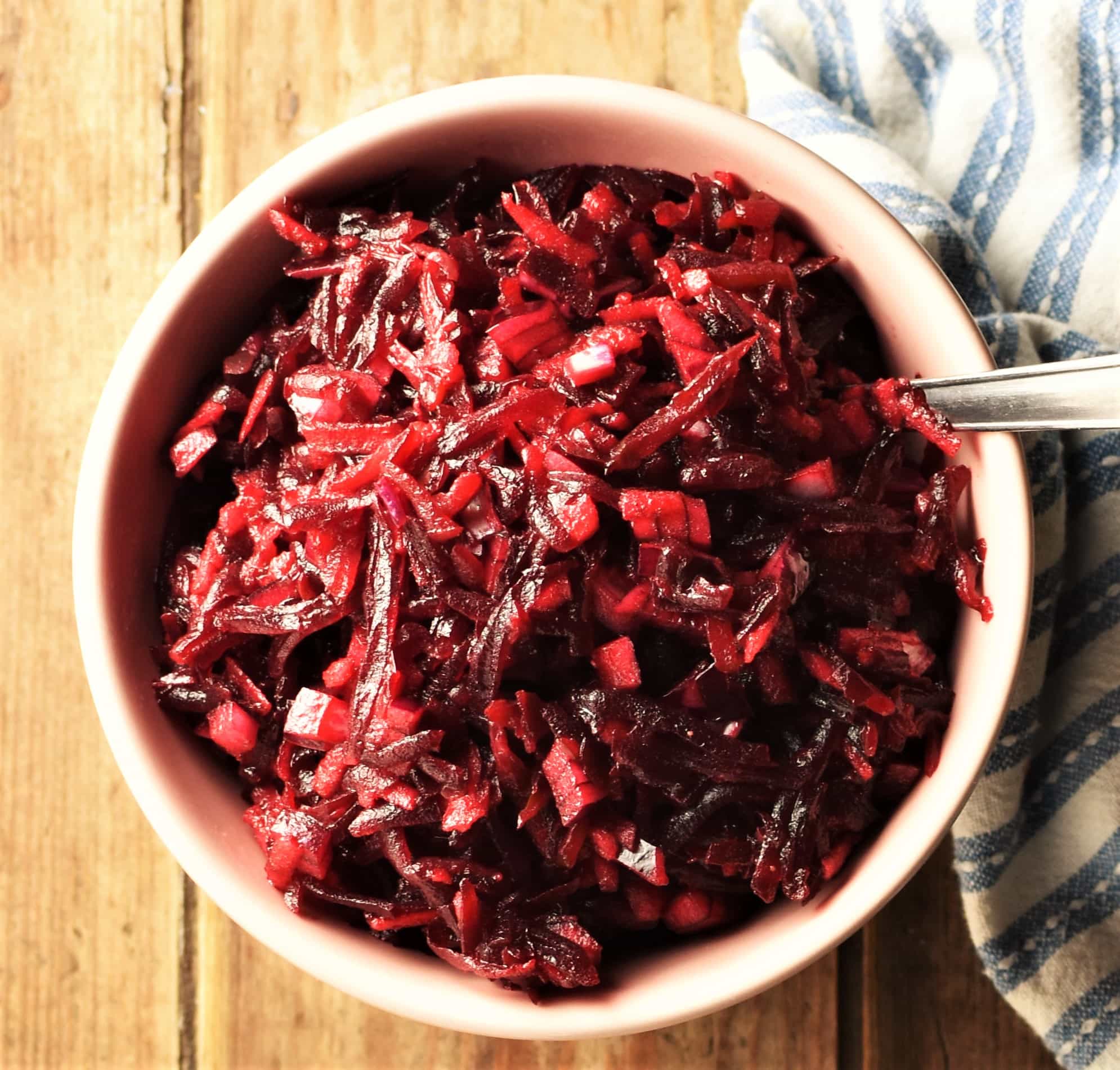 Top down view of shredded beet salad in pink bowl with spoon.
