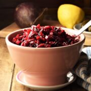 Side view of beetroot slaw in pink bowl with spoon, with lemon and beetroot in background.