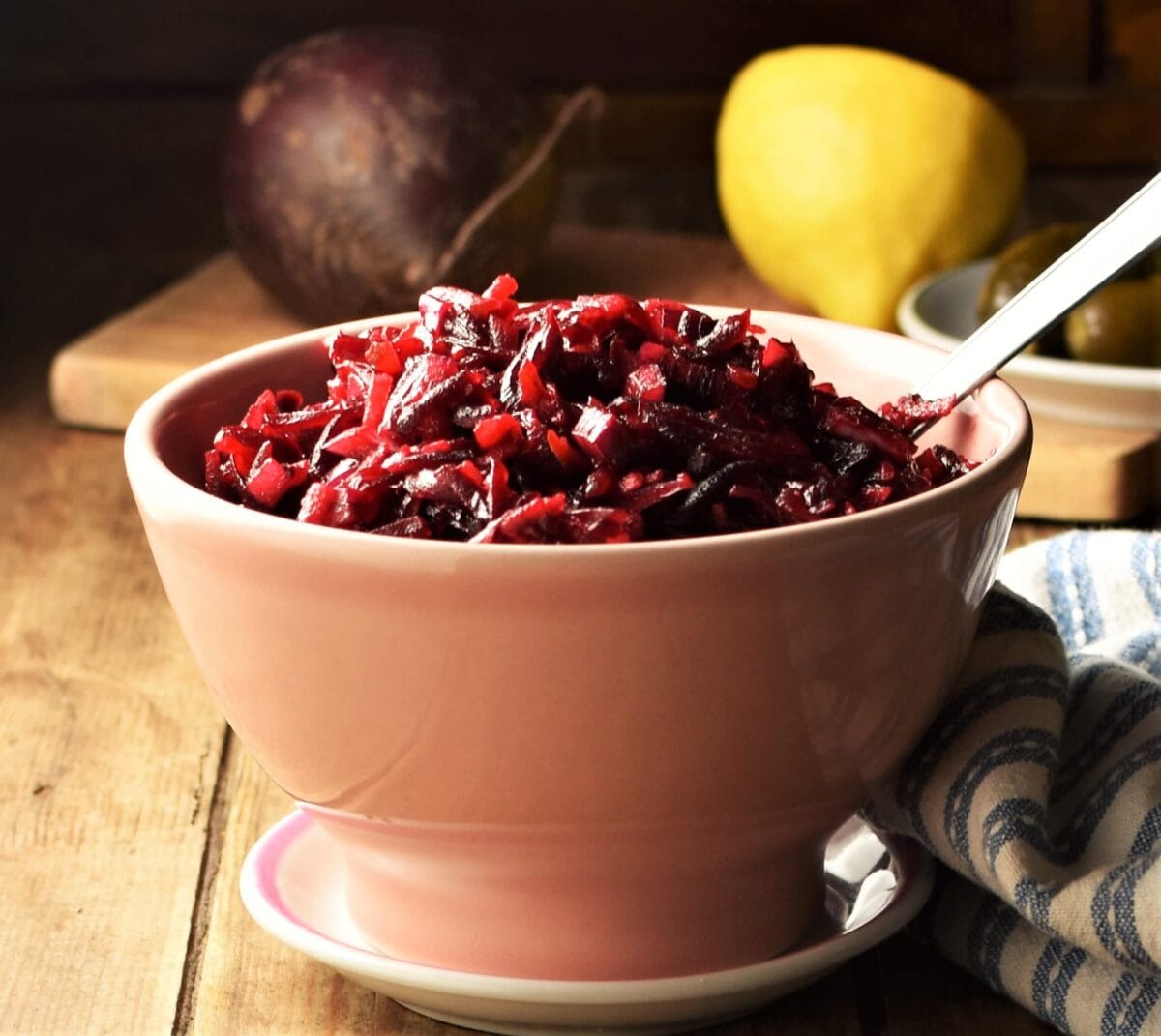 Side view of beetroot slaw in pink bowl with spoon, with lemon and beetroot in background.