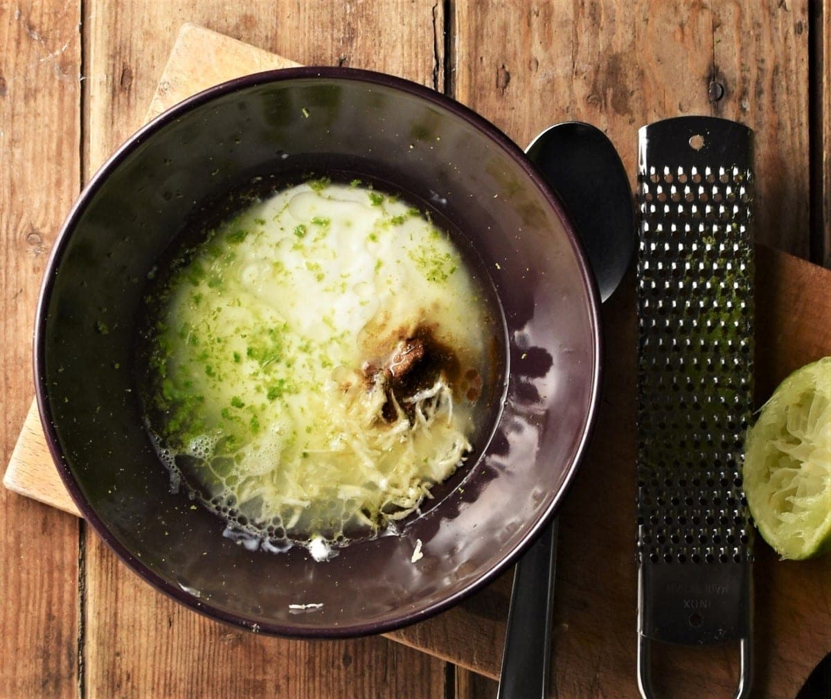 Salad dressing mixture in purple bowl with fruit zester and lime in background.