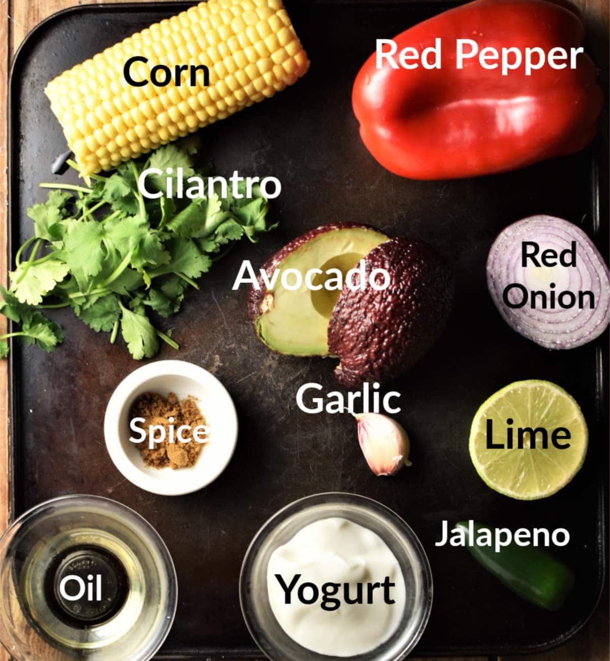Corn salsa ingredients with labels in individual dishes on top of dark tray.
