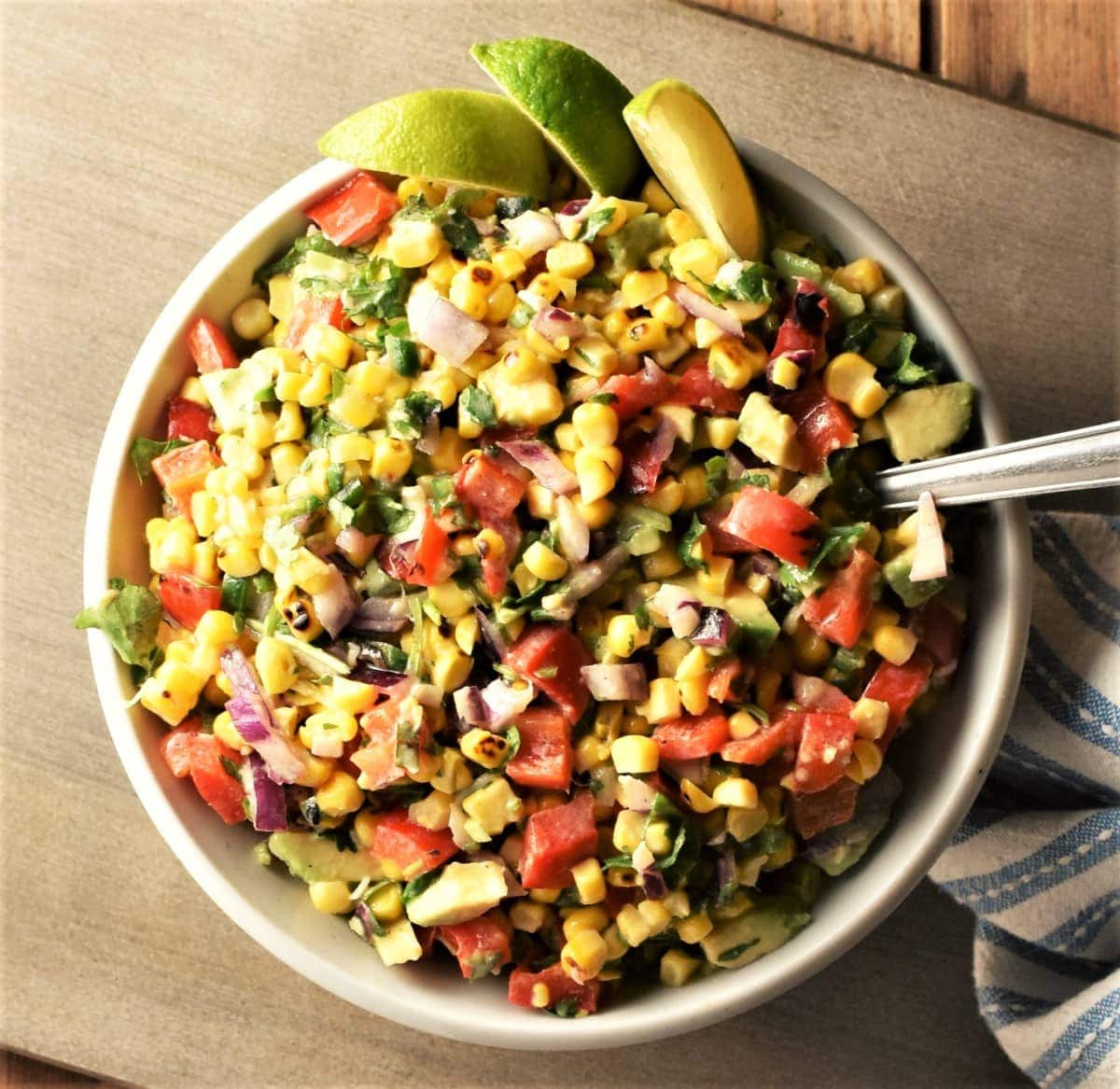 Top down view of corn salsa with lime wedges in bowl with spoon.