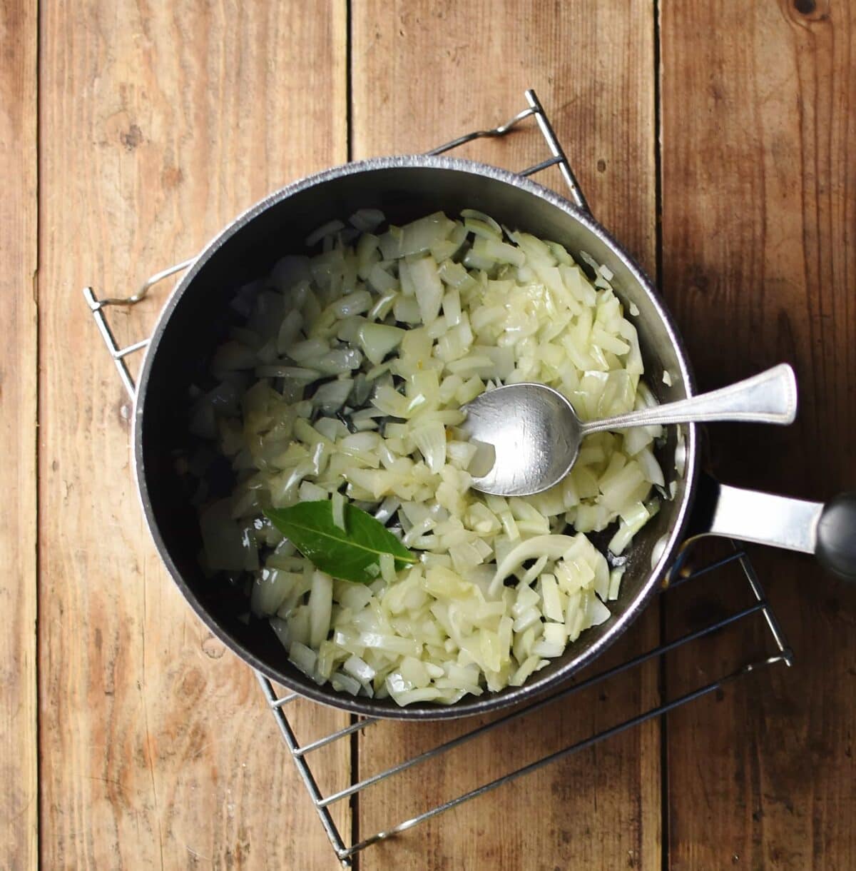Chopped onions and bay leaf inside large pot with spoon.