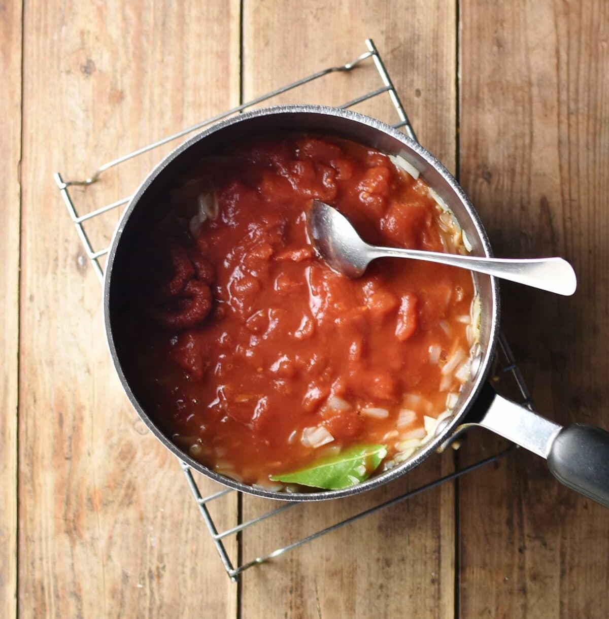 Tomato sauce with bay leaf and spoon in large saucepan.