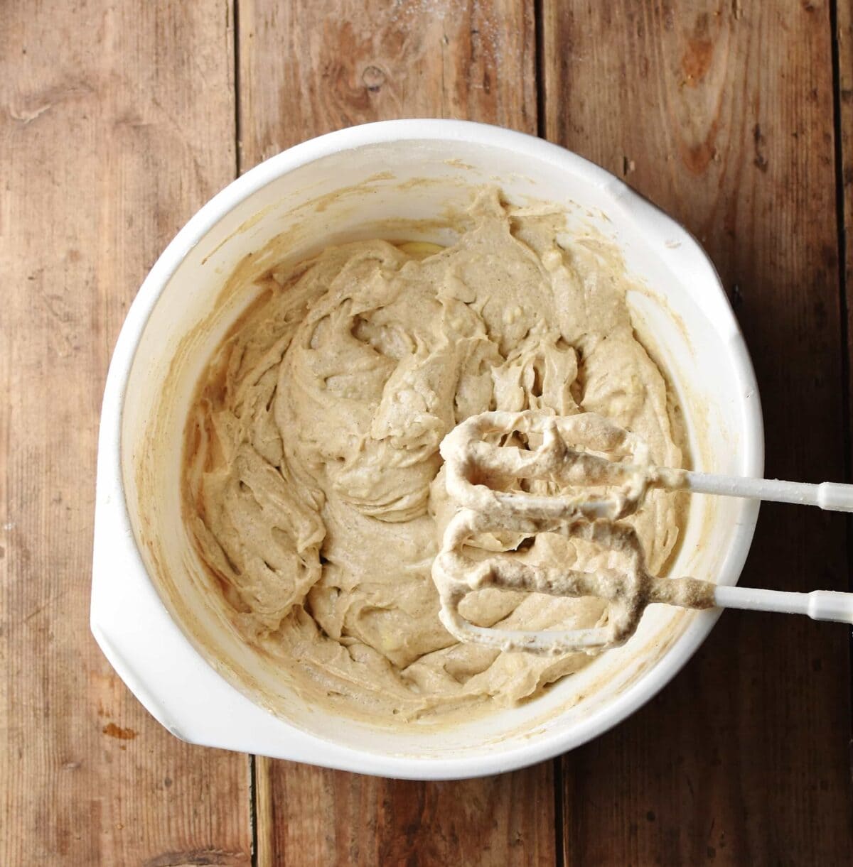 Pumpkin spice cupcake batter in large white bowl with electric mixer ends.