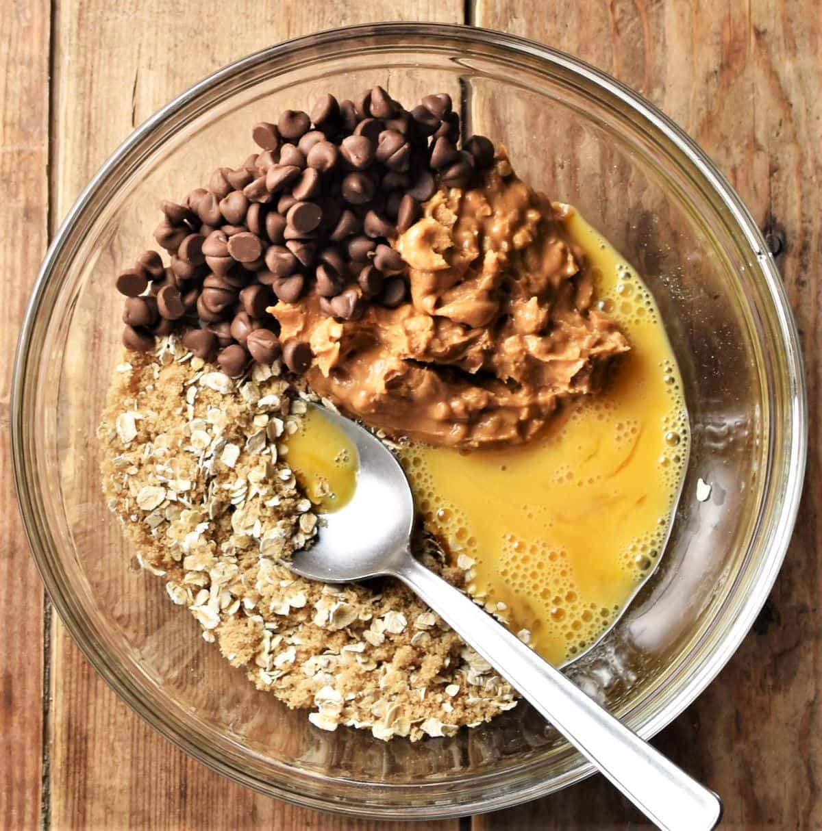 Oats, egg, peanut butter and chocolate chips in mixing bowl with spoon.