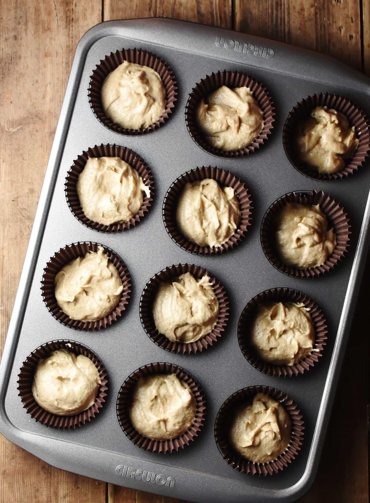 Cupcake batter in 12 brown liners in muffin pan.