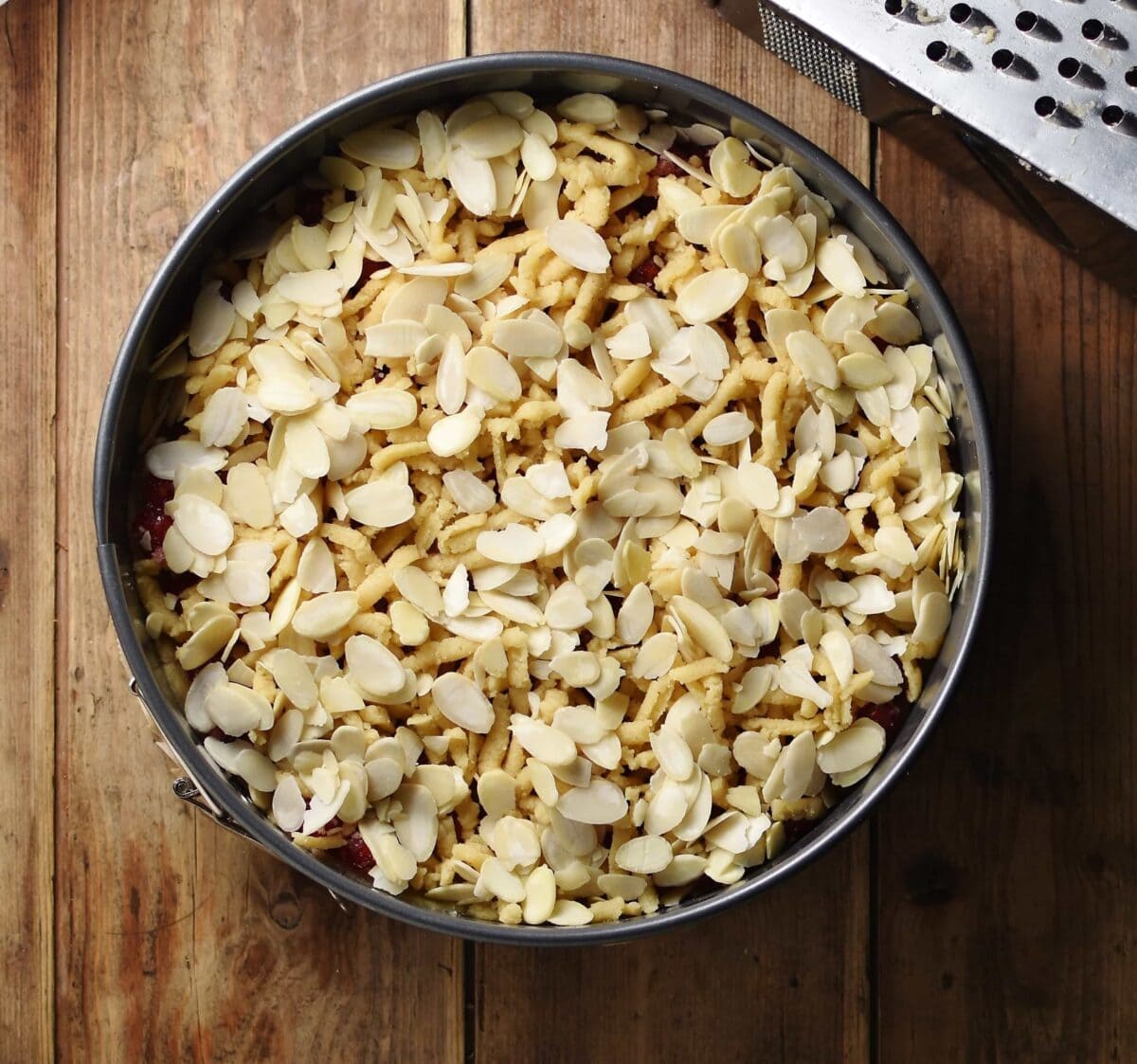 Unbaked cake in round tin with almond flakes on top.