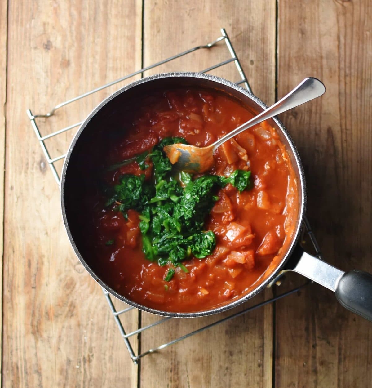 Tomato sauce with spinach mixture in large pot with spoon.