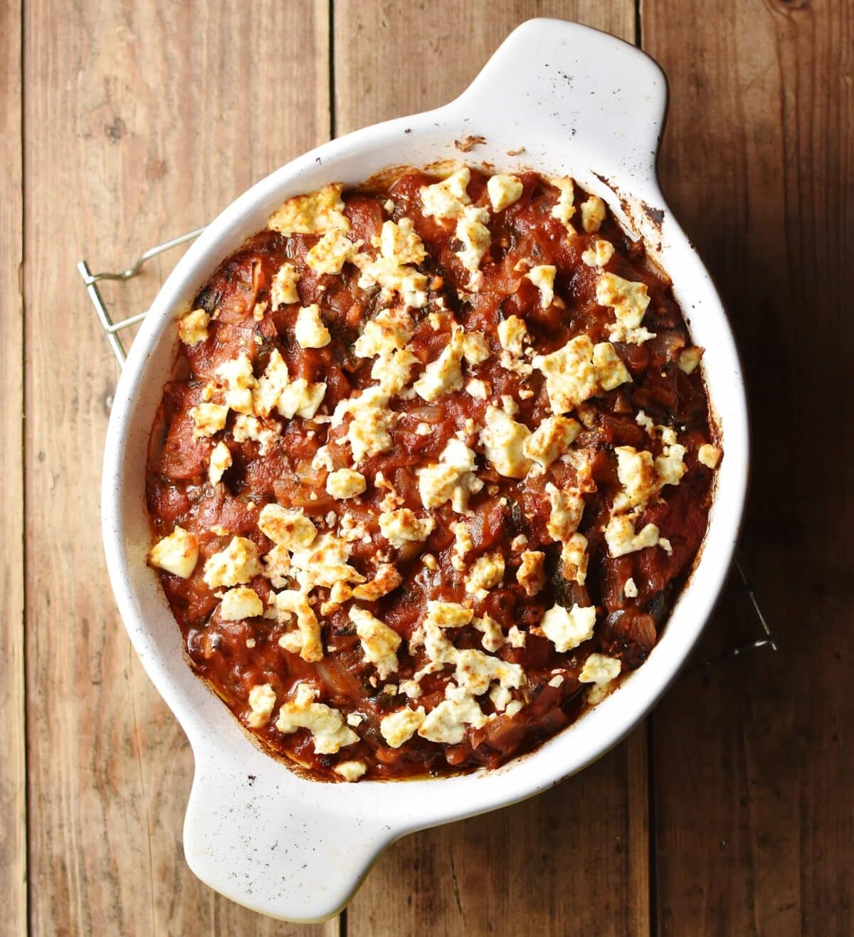 Tomato casserole with crumbled feta on top inside white oval dish.