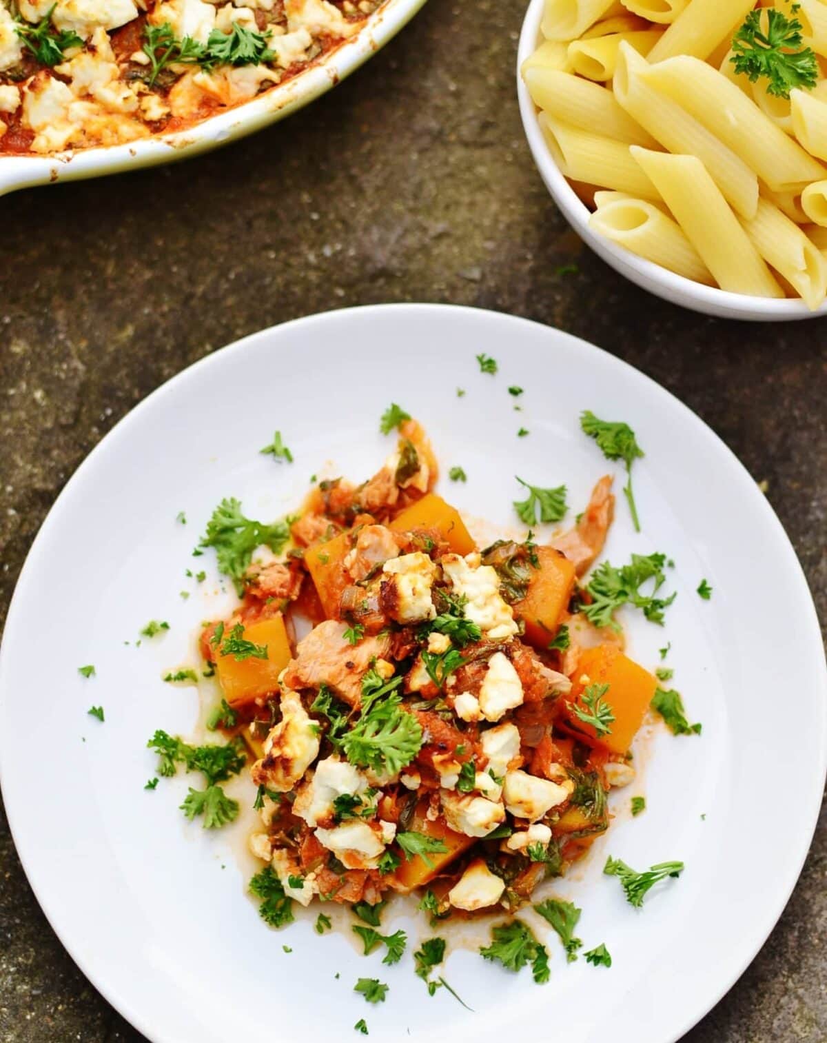 Tuna bake with butternut squash, spinach and feta on white plate with partial view of white bowl with pasta and casserole dish.