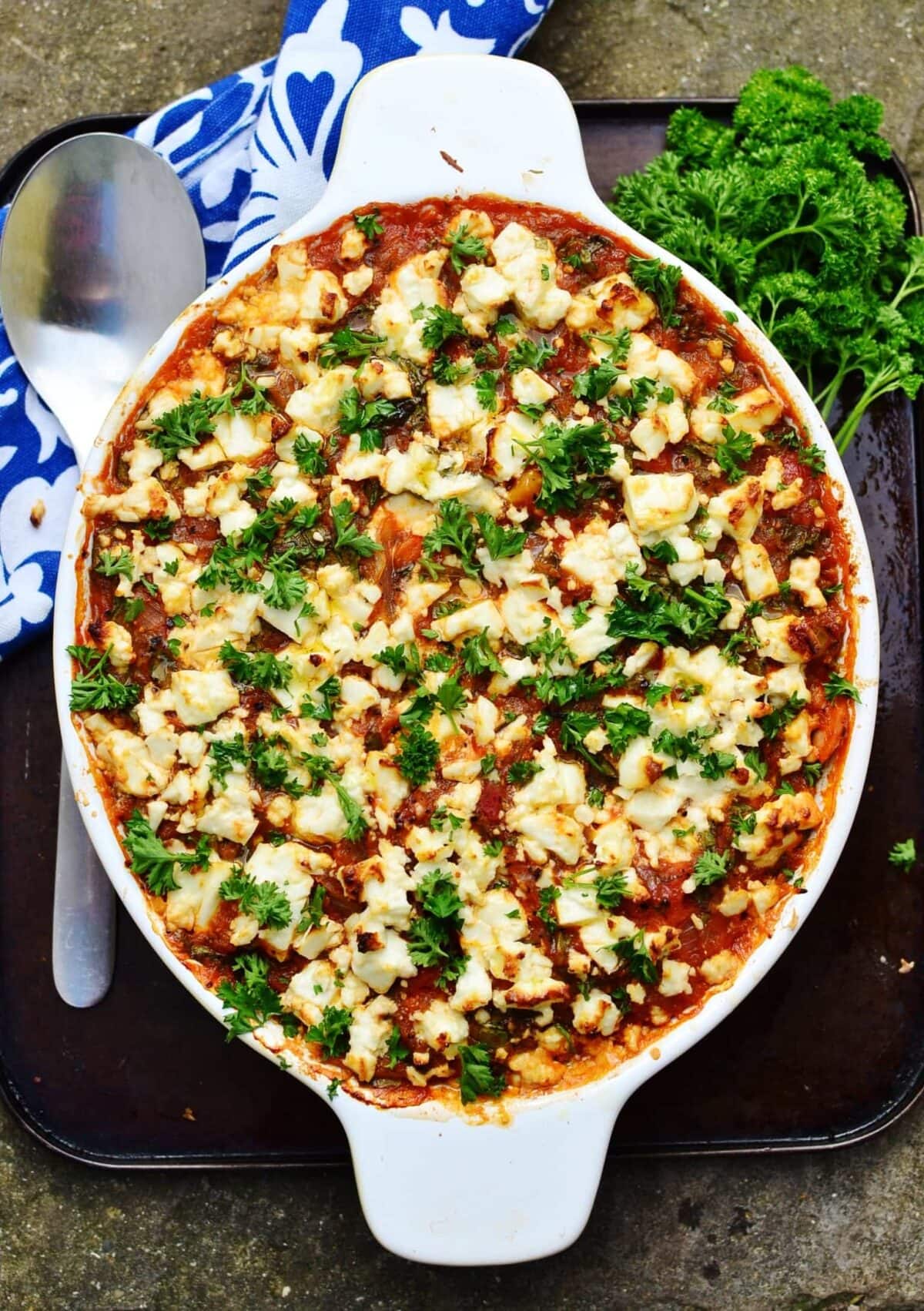 No pasta tuna bake in white oval casserole dish with spoon, blue-and-white cloth and parsley on oven tray.