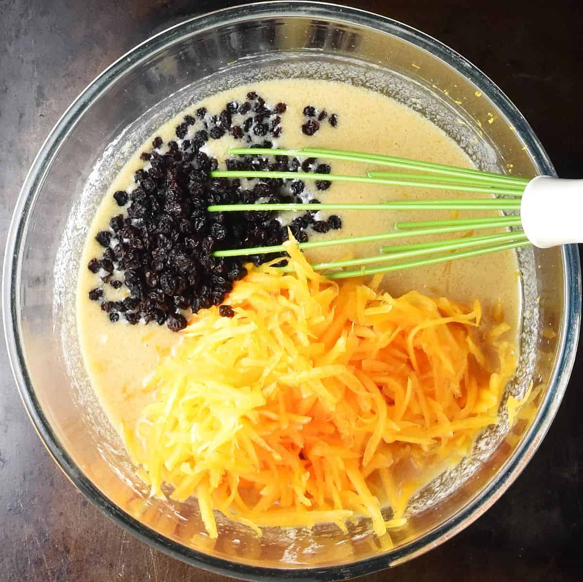 Shredded squash and currants in muffin batter in mixing bowl with whisk.