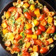Top down view of pasta with chunks of butternut squash and tomato in pan.