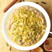 Top down view of chai oatmeal topped with passion fruit in white bowl with spoon.