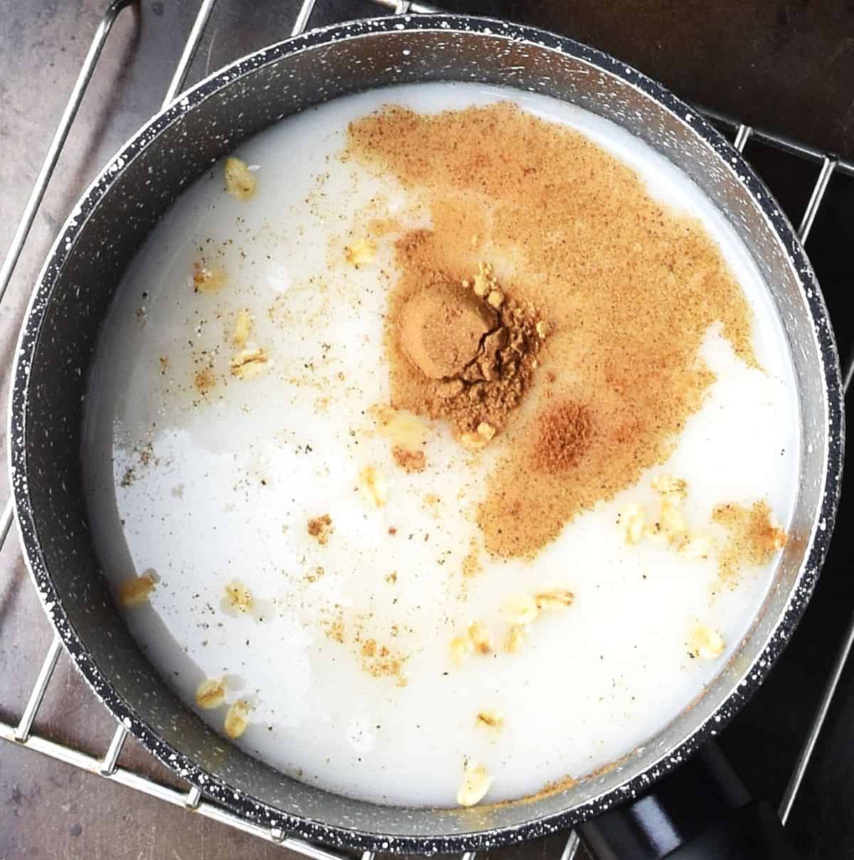 Top down view of oats, milk and spices for oatmeal in black pot.