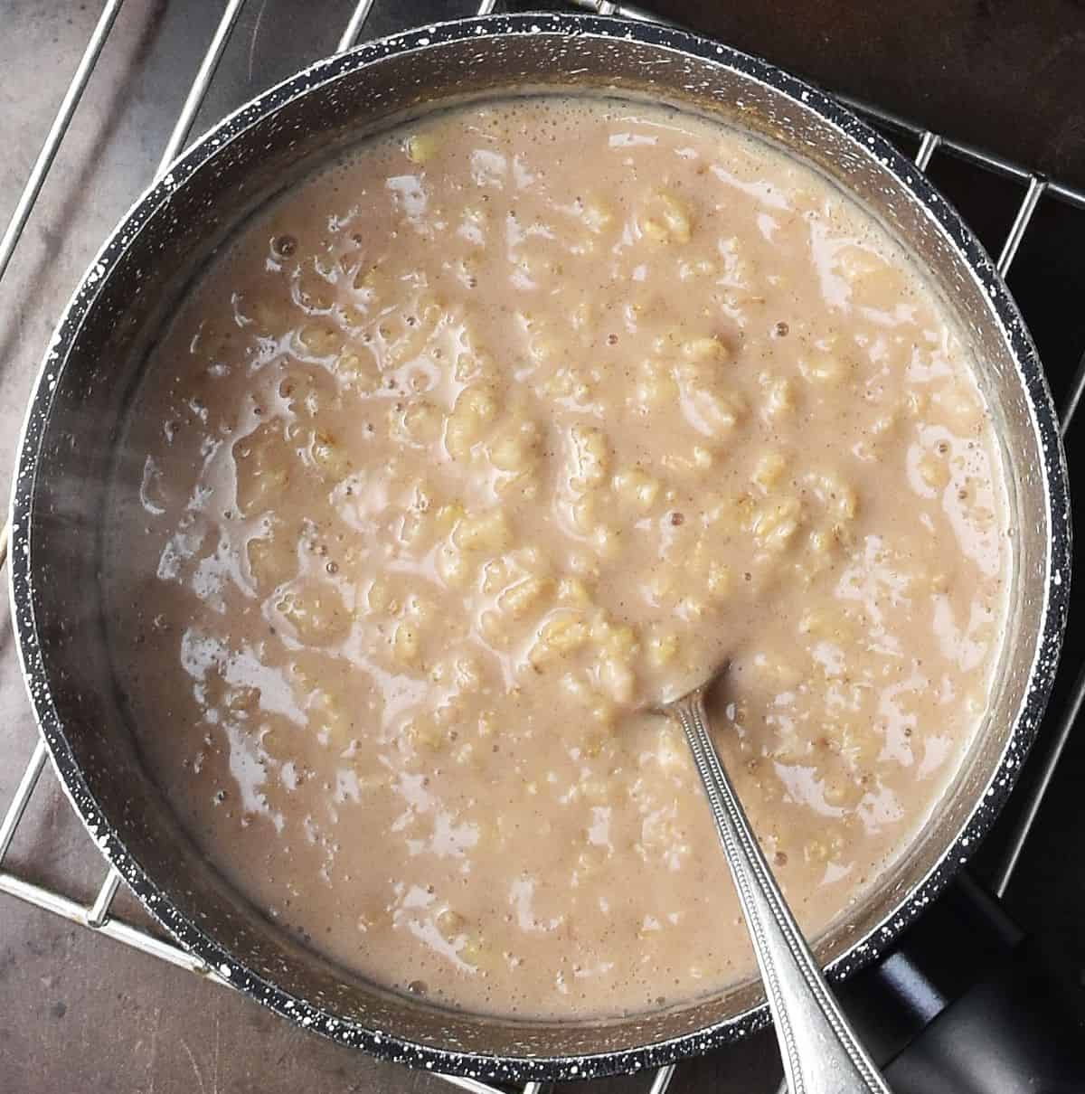 Top down view of creamy oatmeal with chai spices in black pot with spoon.