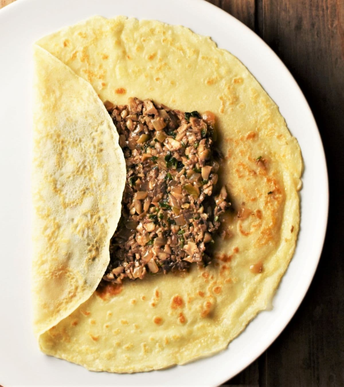 Folding crepes with mushroom filling on top of plate.