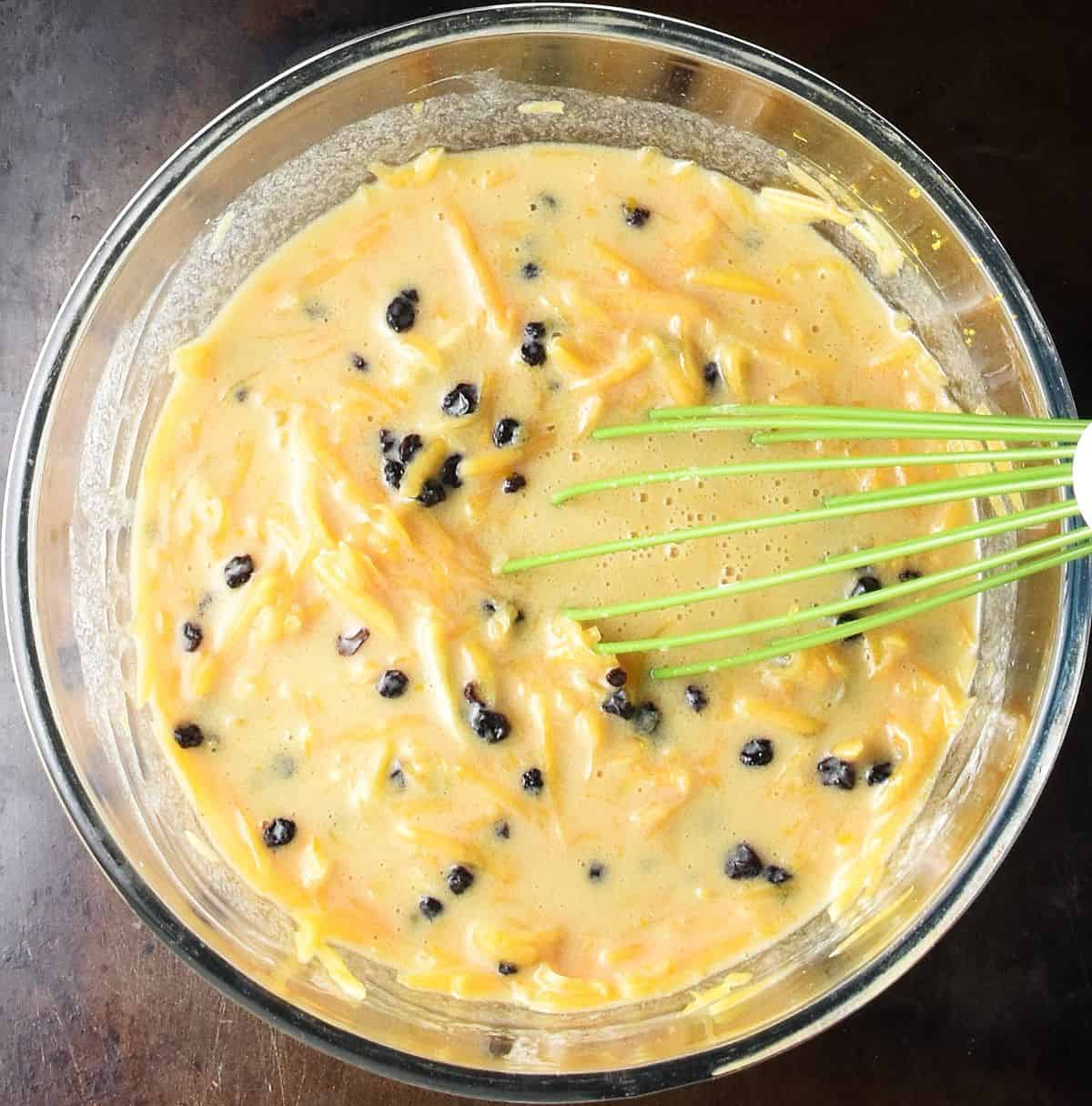 Top down view of fresh squash wet muffin mixture in glass bowl with whisk.
