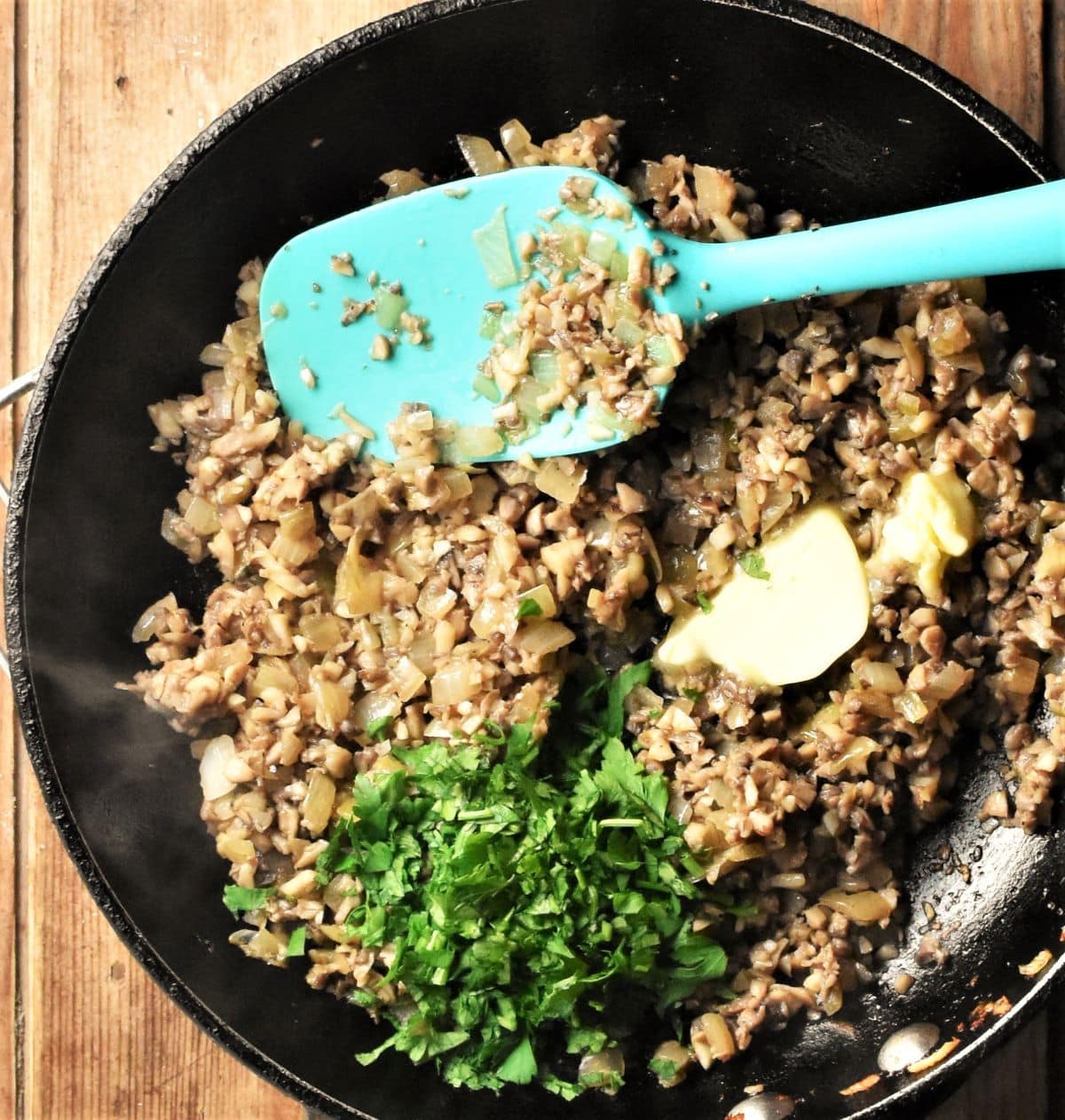 Frying chopped mushrooms with parsley and butter in large pan with blue spoon.
