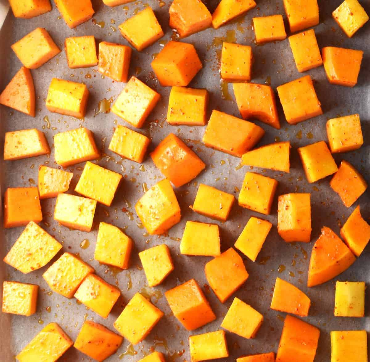 Cubed squash with seasoning on top of parchment.