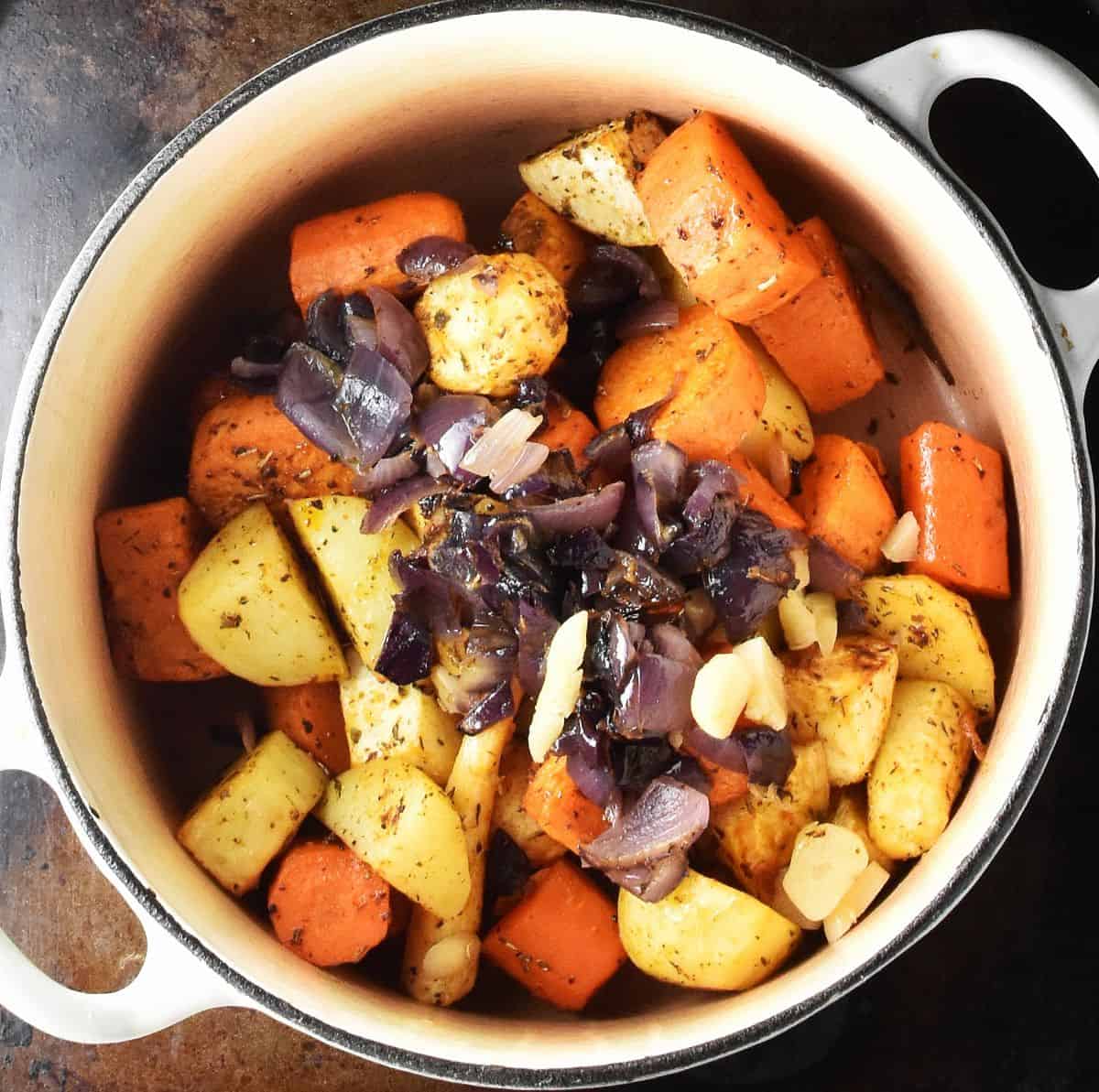 Roasted root vegetables with chopped red onion on top in white pot.