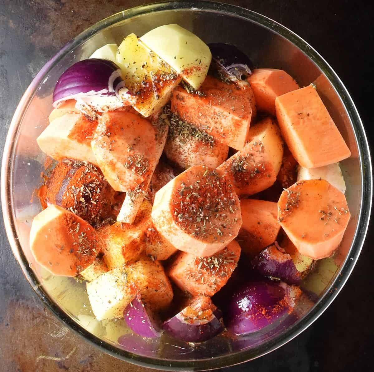 Pieces of peeled root vegetables with herbs in glass bowl.