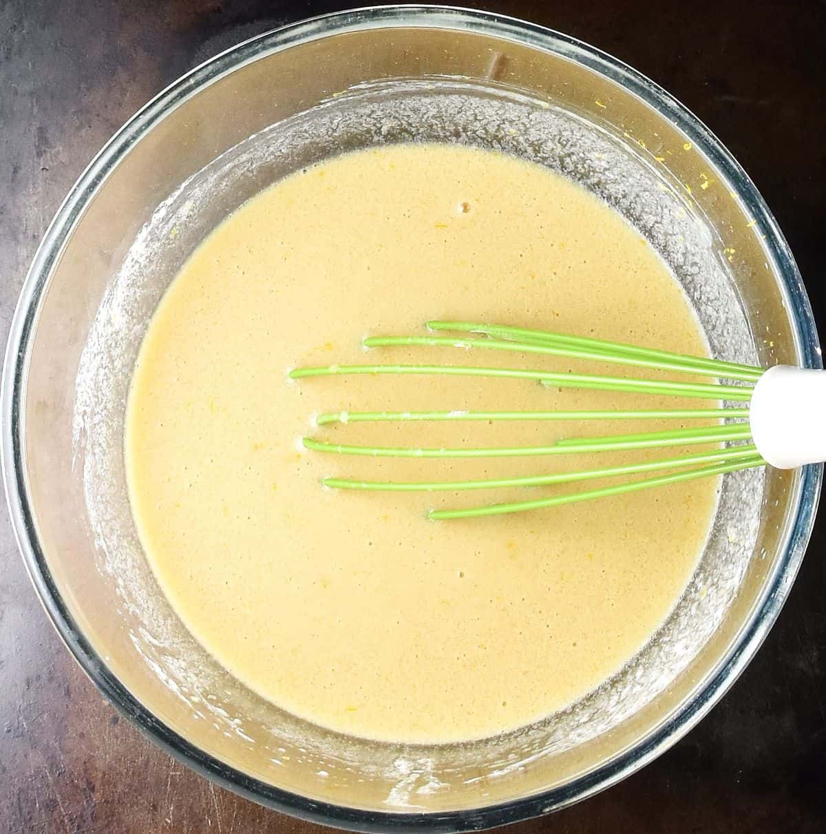 Creamy mixture in glass bowl with green whisk.