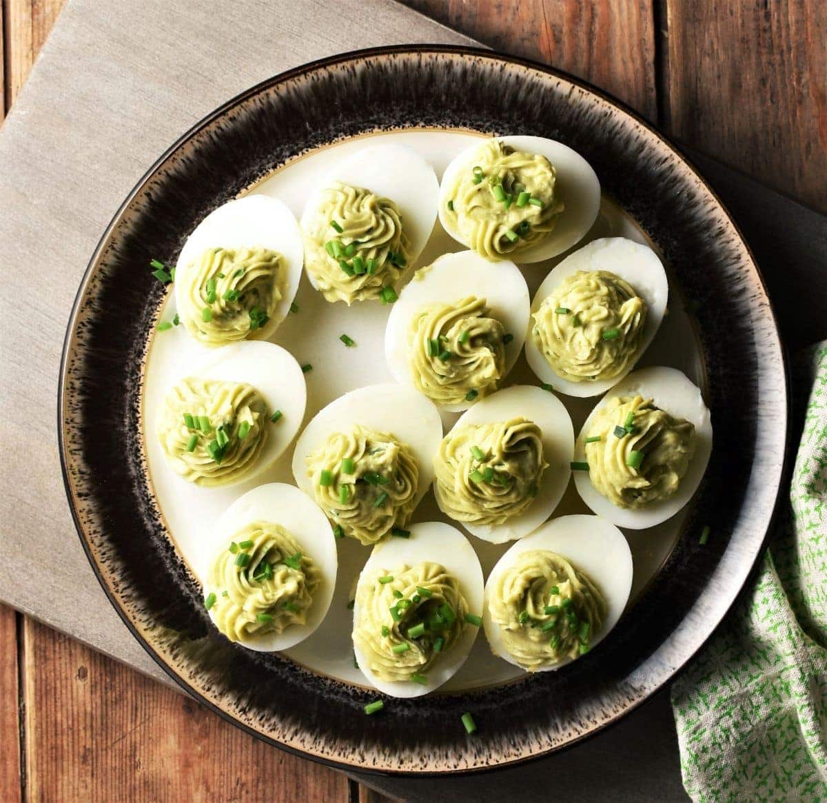 Top down view of avocado devilled eggs on top of brown rimmed plate.