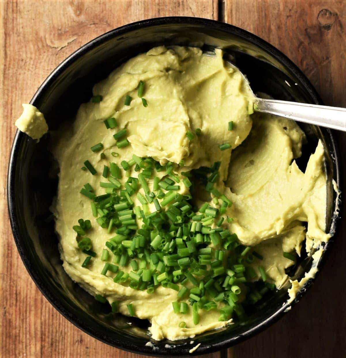 Creamy deviled eggs filling with chives in black bowl with spoon.