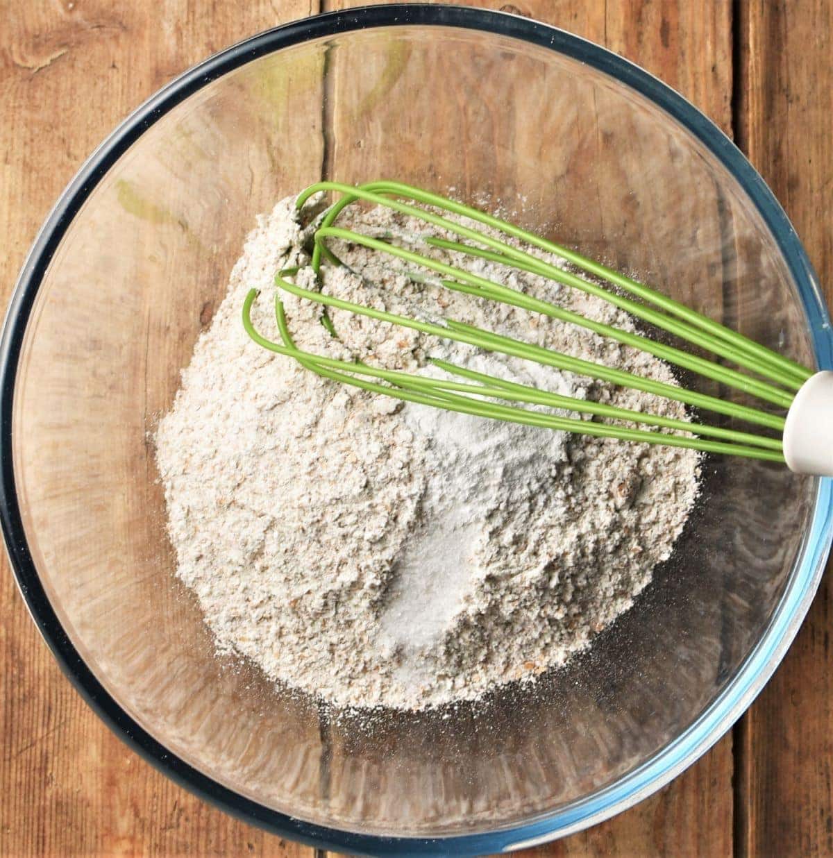 Dry ingredients for breadsticks in mixing bowl with green whisk.