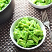 Top down view of spinach macaroni cheese in white bowl, with fork to right and more macaroni cheese in bowl and saucepan at top.
