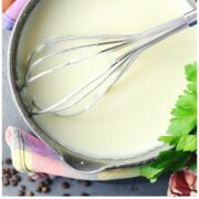 White sauce in pot with metal whisk and spices in background.