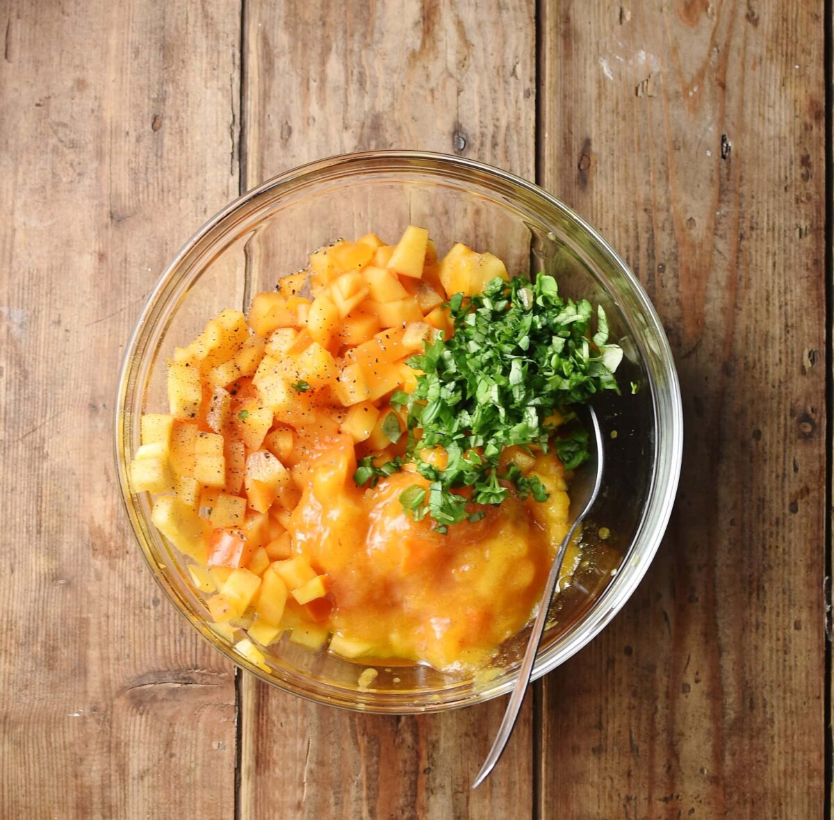 Chopped persimmon with herbs in mixing bowl with spoon.