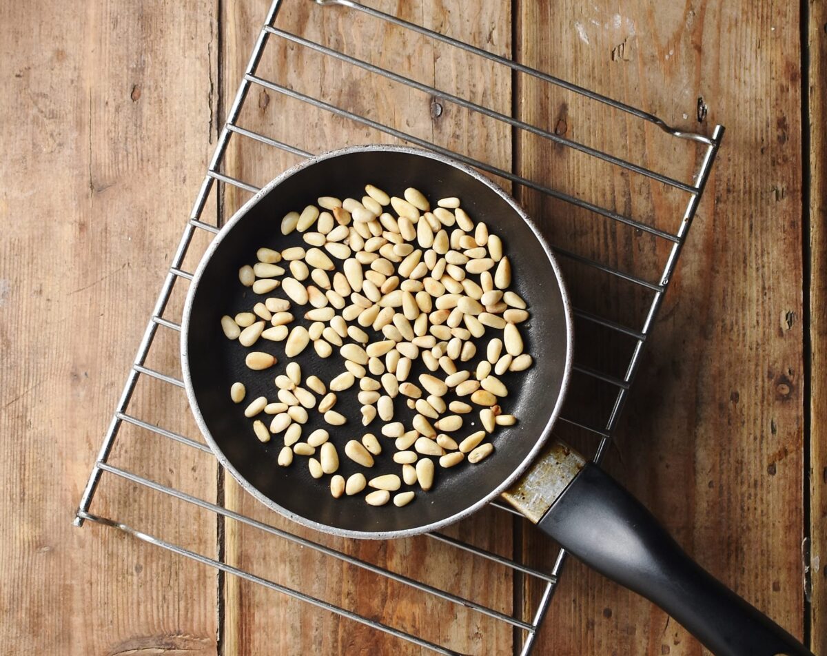 Pine nuts in small pan on rack.