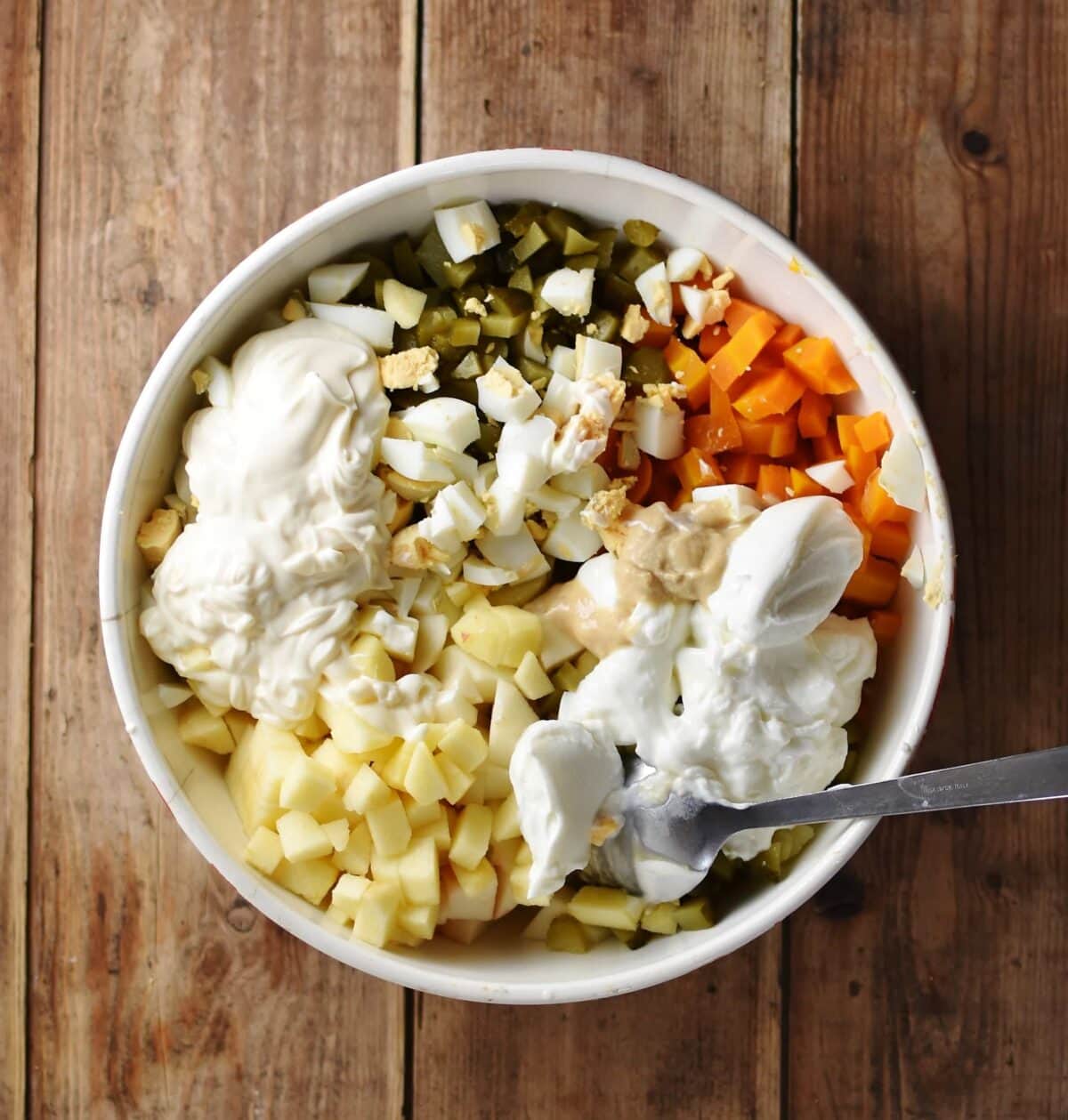 Chopped vegetables and yogurt inside large bowl with spoon.