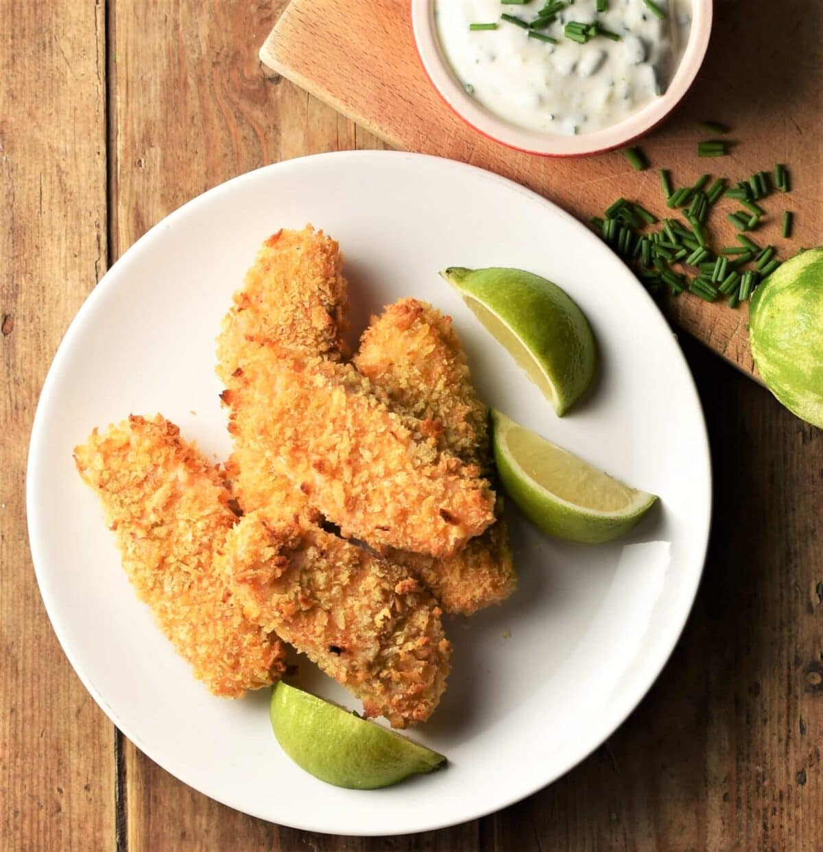 Breaded salmon fish fingers on top of plate with lime wedges.