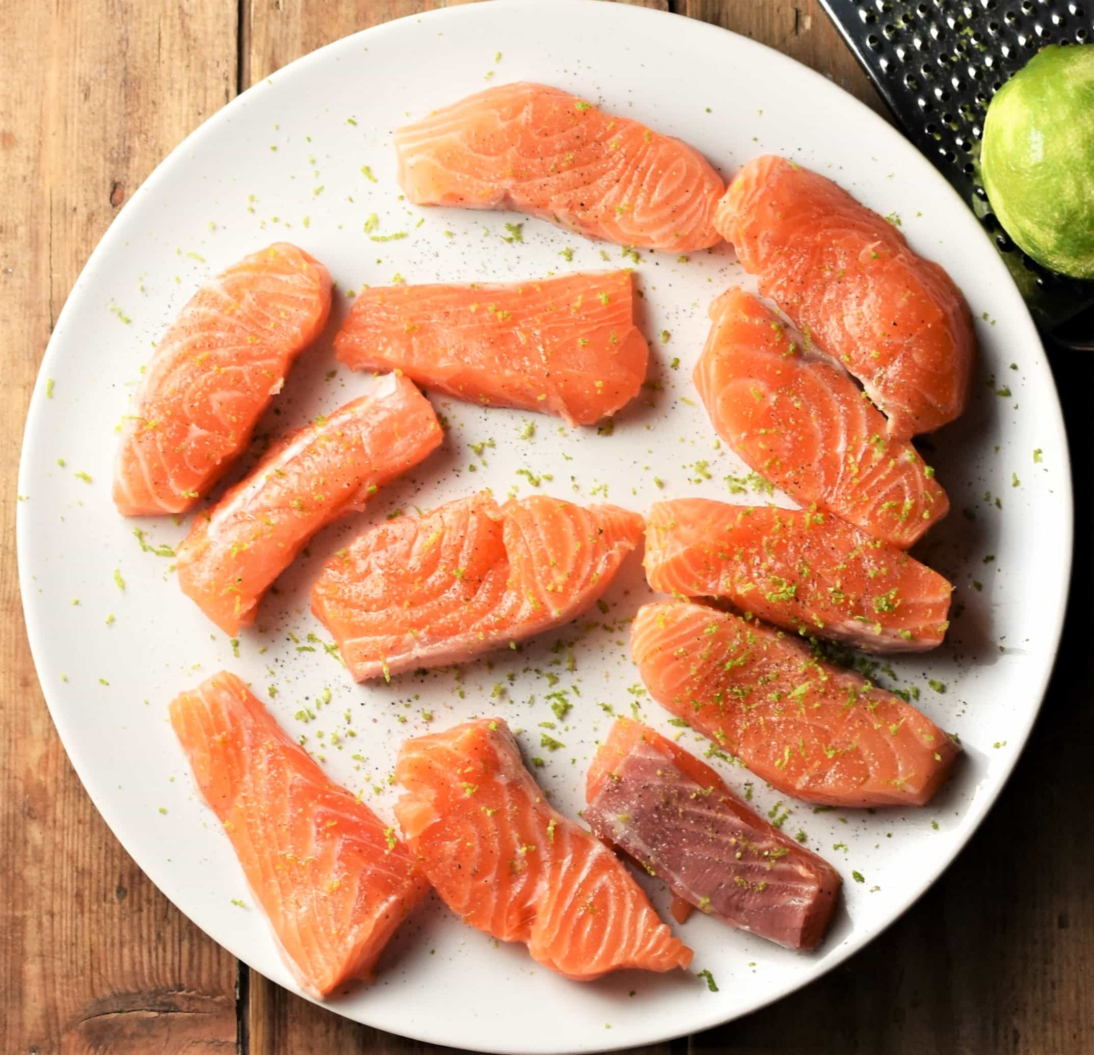 Raw salmon pieces with lime zest on top of white plate.