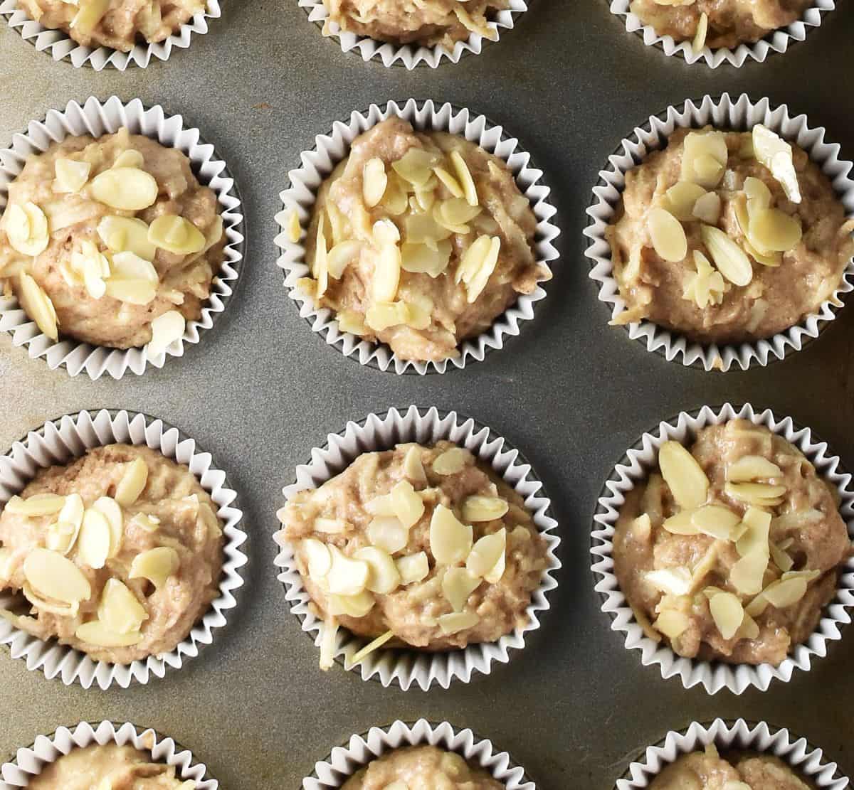 Gluten free apple muffin batter with almond flakes on top on muffin pan.