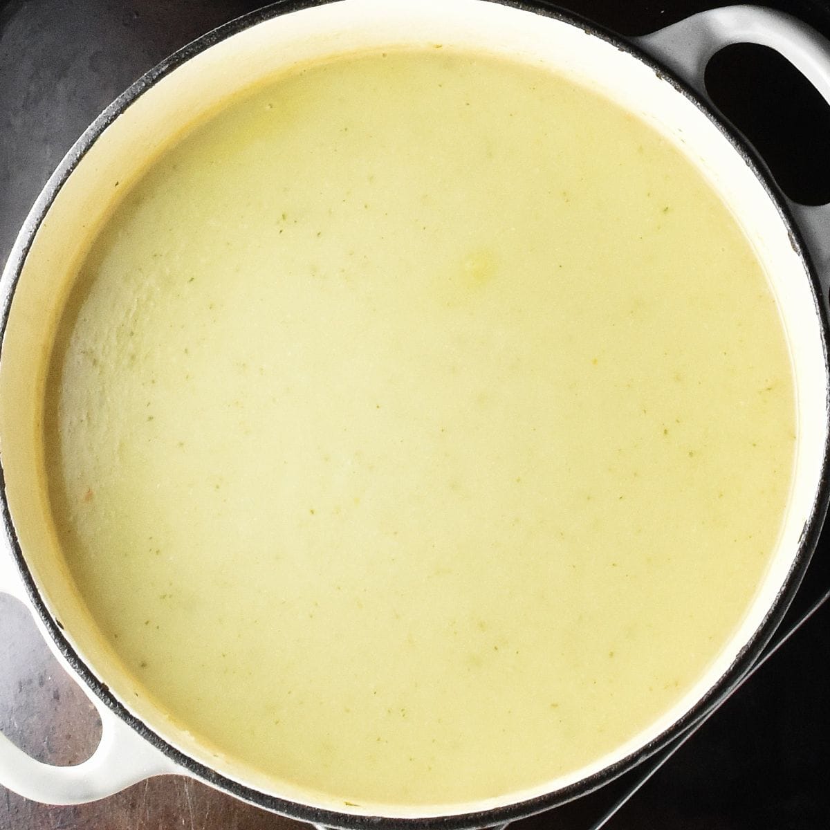 Top down view of creamy cauliflower leek potato soup in large white pot.
