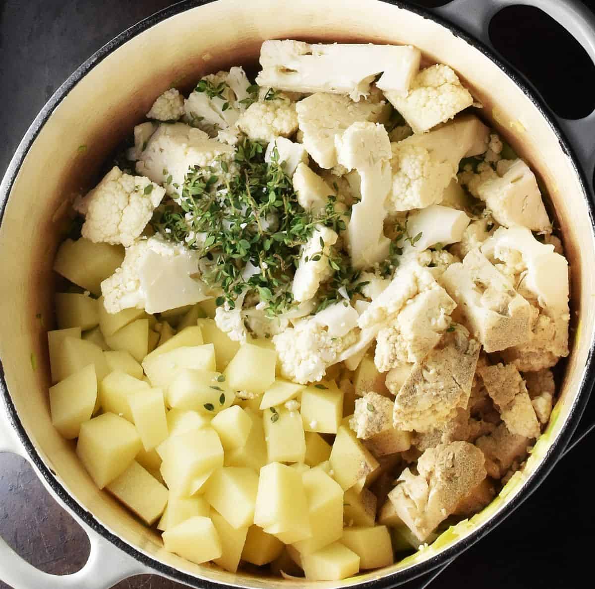 Cubed potatoes and cauliflower with chopped herbs in white pot.