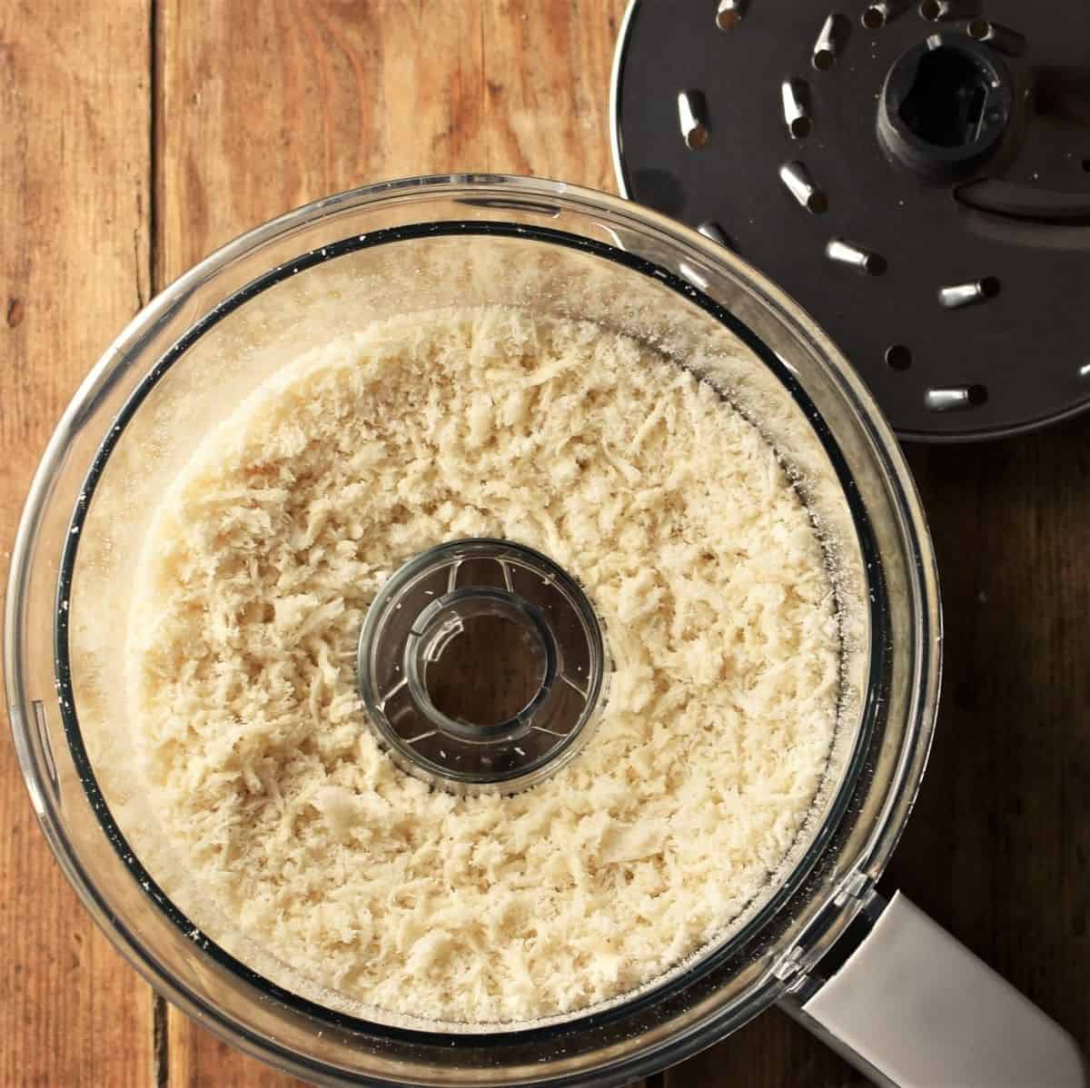 Panko breadcrumbs in food processor bowl and grating disc in background.