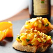 Side view of persimmon bruschetta slices with bottle of balsamic vinegar in back.